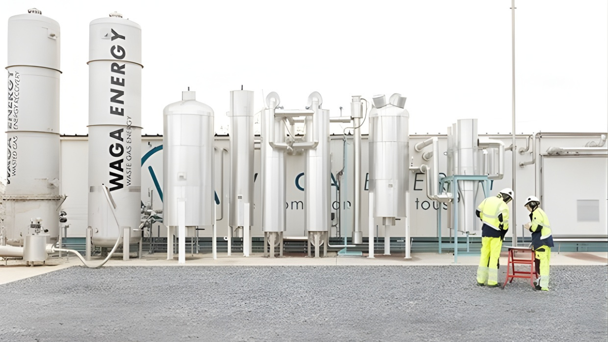 Renewable gas processing facility with tall white cylinders and workers in safety gear